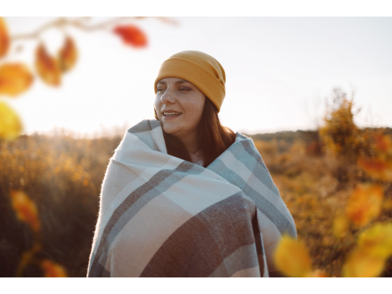 Woman outdoors wearing a promotional picnic blankets during a cozy fall event, showcasing custom logo and fleece design.